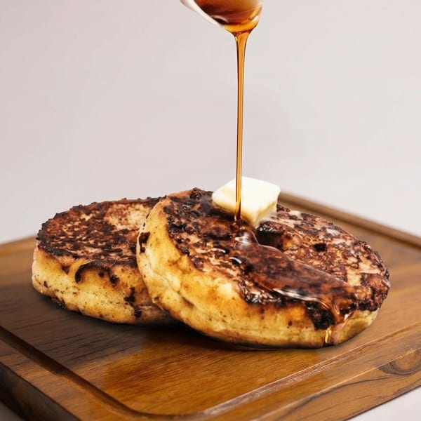Golden syrup pouring over two round, toasted French toast slices with melting butter on a wooden board.