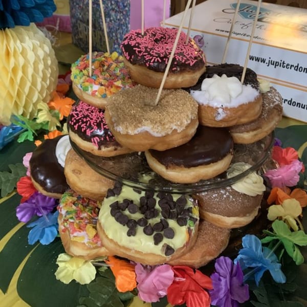 A tiered display of Rockstar Donuts, featuring various colorful toppings, surrounded by tropical decorations.